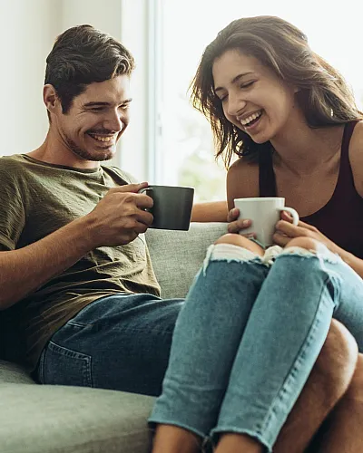 Cozy living room setting with a cheerful couple enjoying coffee on a stylish gray sofa, bathed in warm natural light.