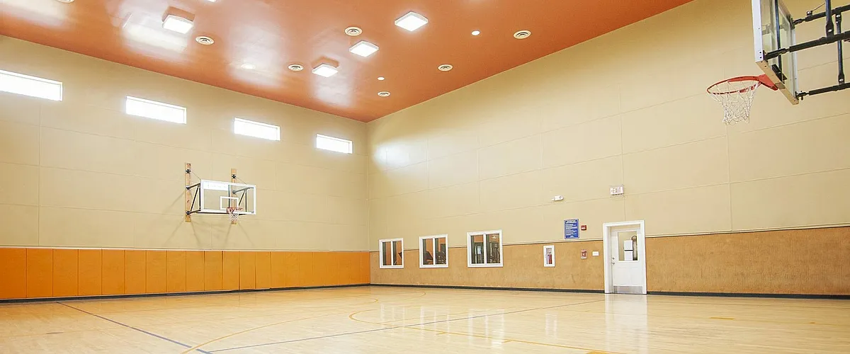Spacious indoor basketball court with sleek wooden flooring, vibrant orange accents, and modern lighting, perfect for sports enthusiasts.