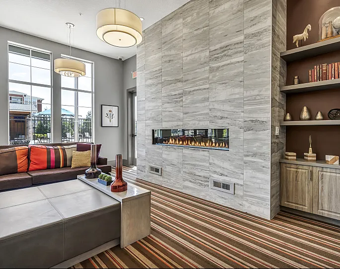 Elegant apartment living room boasting a modern linear fireplace, stylish shelving, and abundant natural light through large windows, complemented by vibrant decor and sophisticated design.