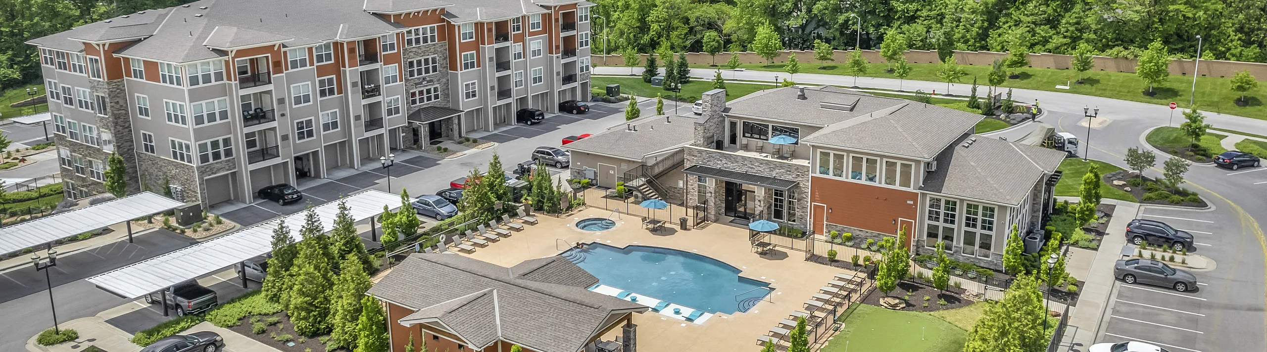 Modern apartment complex with spacious courtyard, luxurious pool, and vibrant green surroundings under a clear blue sky.