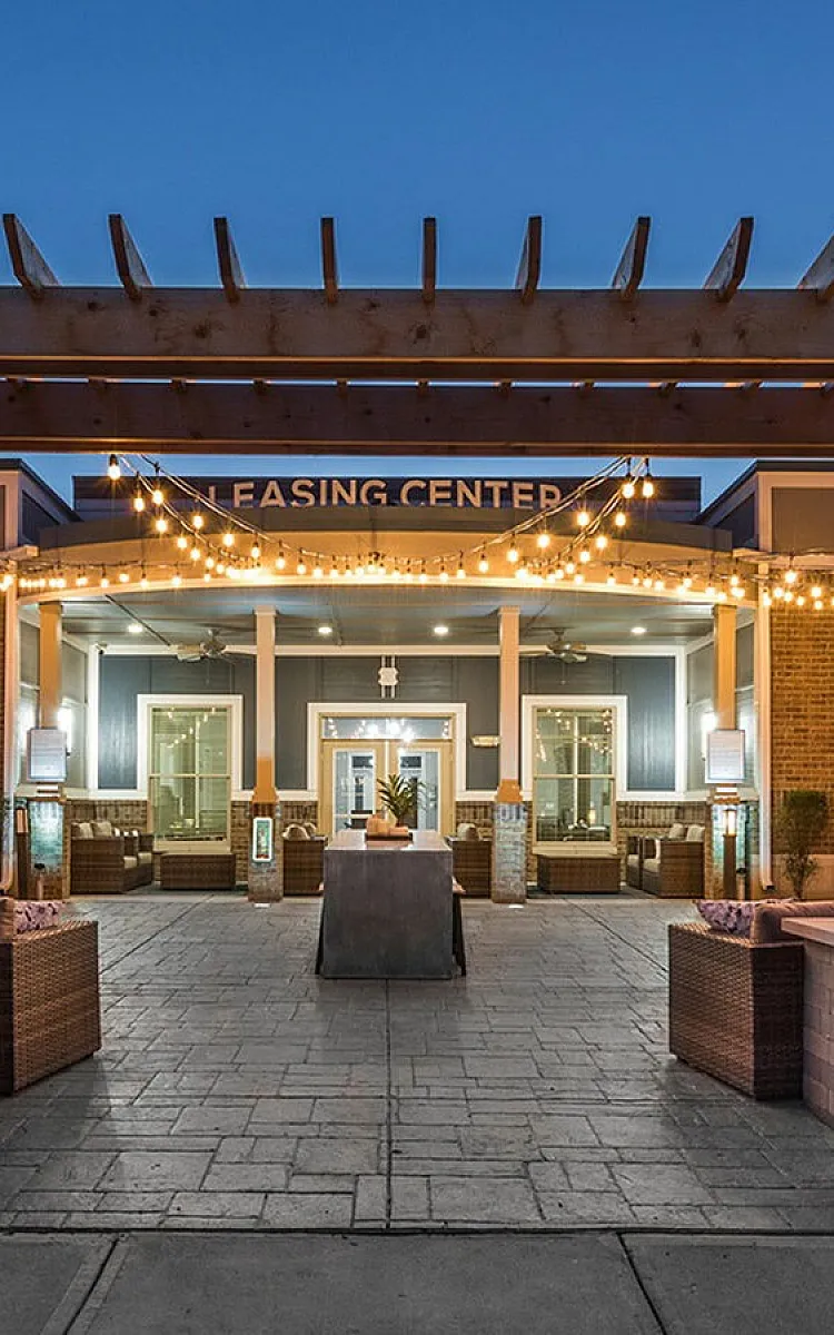 Charming leasing center entrance with string lights and cozy outdoor seating, perfect for welcoming residents.