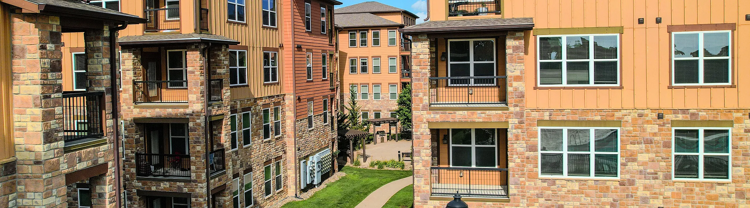 Charming modern apartment complex with vibrant facades, stone accents, and lush green walkways under a clear blue sky.