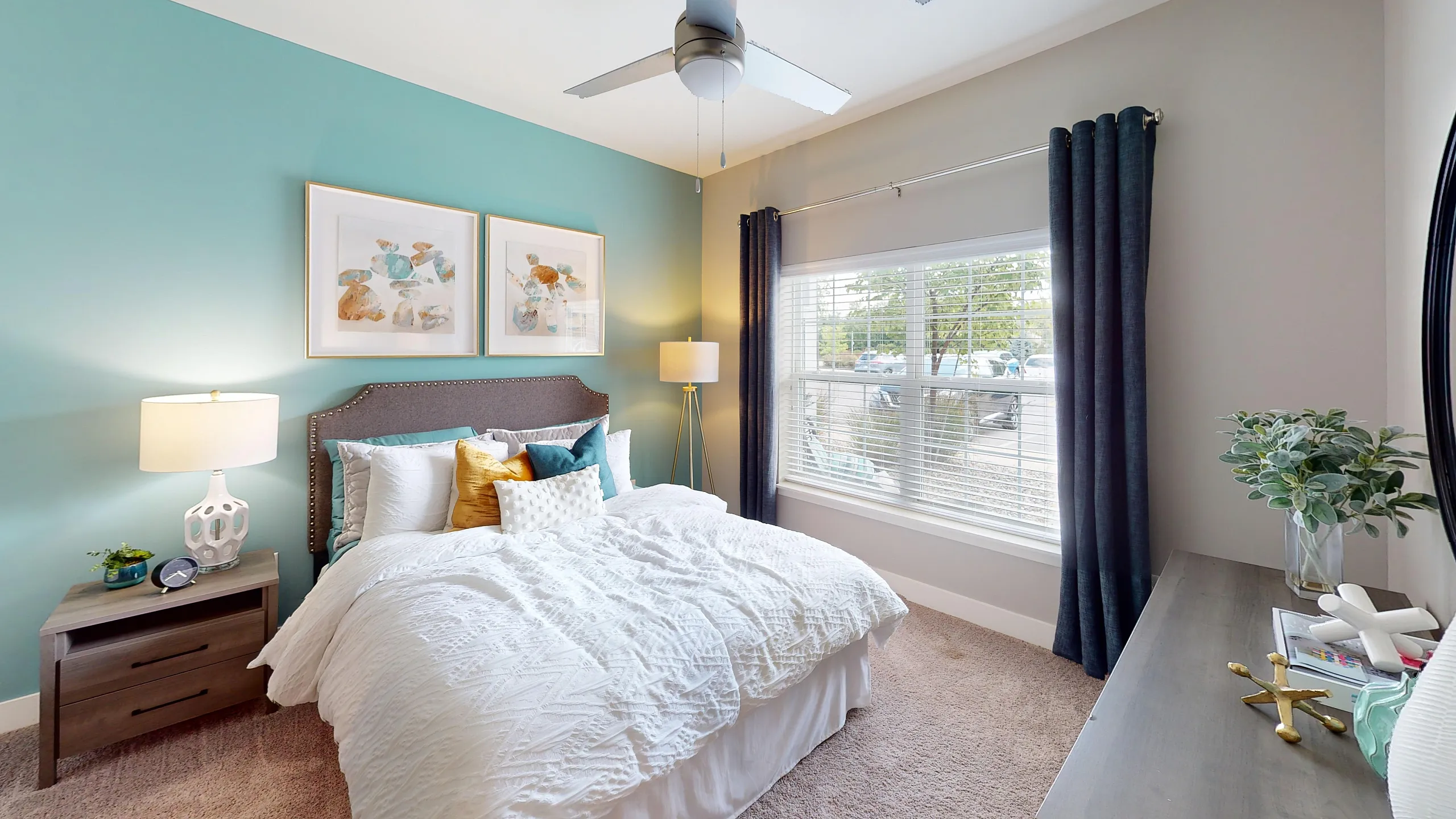 Elegant bedroom with teal accent wall, cozy bed, modern decor, and large window allowing natural light.