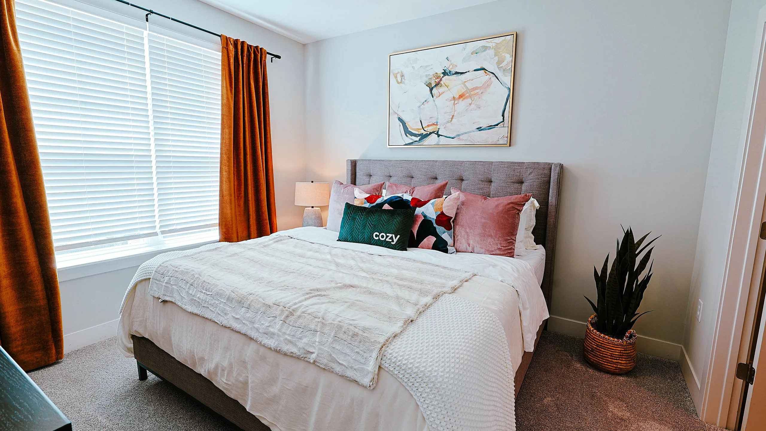 Inviting bedroom featuring a plush bed with stylish pillows, warm natural light, and modern decor.