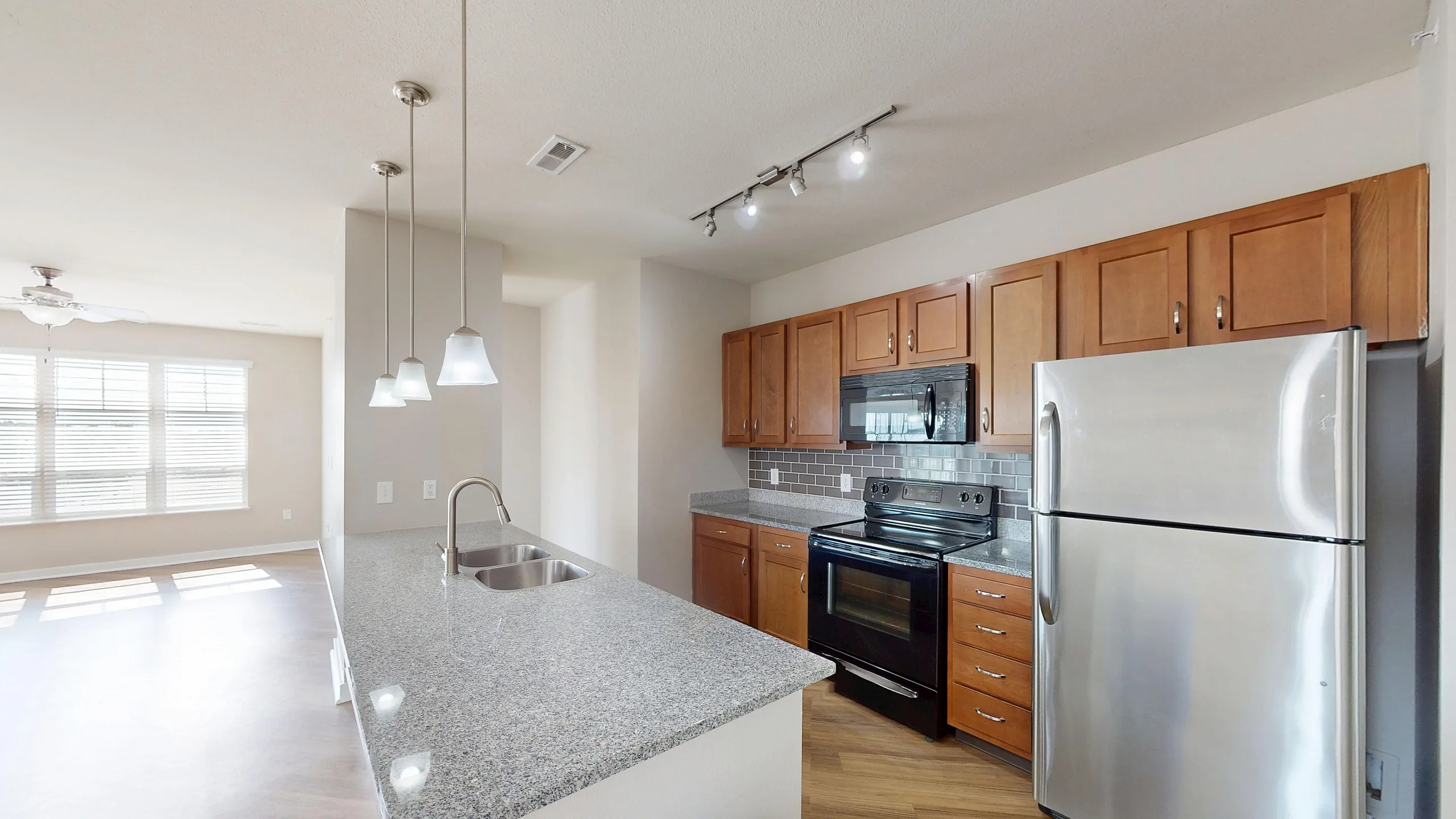 Large and bright open-concept floor plan with pendant lighting, a stainless steel refrigerator, double sink, and black glass-top stove with a microwave range.