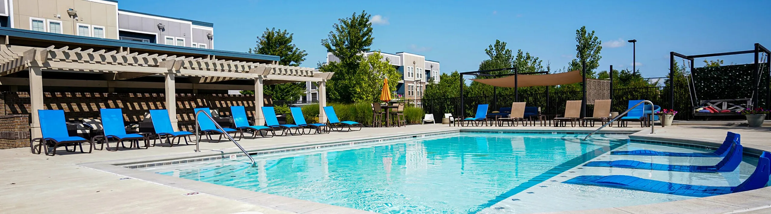 Inviting outdoor pool area with stylish lounge chairs and a pergola, perfect for relaxation in a modern apartment complex setting.