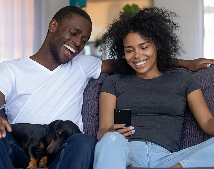 Happy couple relaxing on a cozy sofa, enjoying quality time with a smartphone and pet dog, capturing the essence of comfortable living.