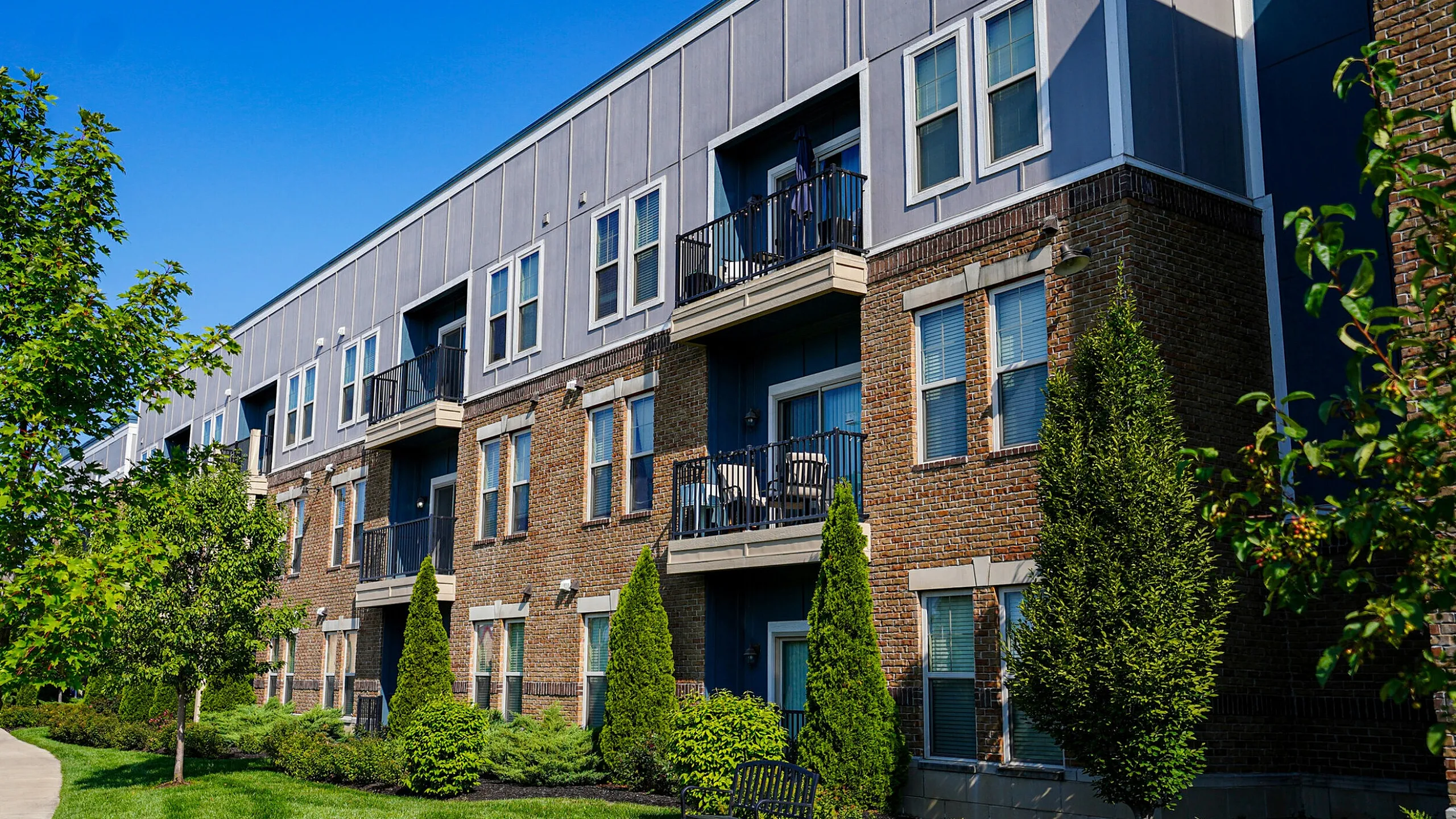 Modern apartment complex with stylish balconies set against a clear blue sky, surrounded by lush greenery for a tranquil living experience.