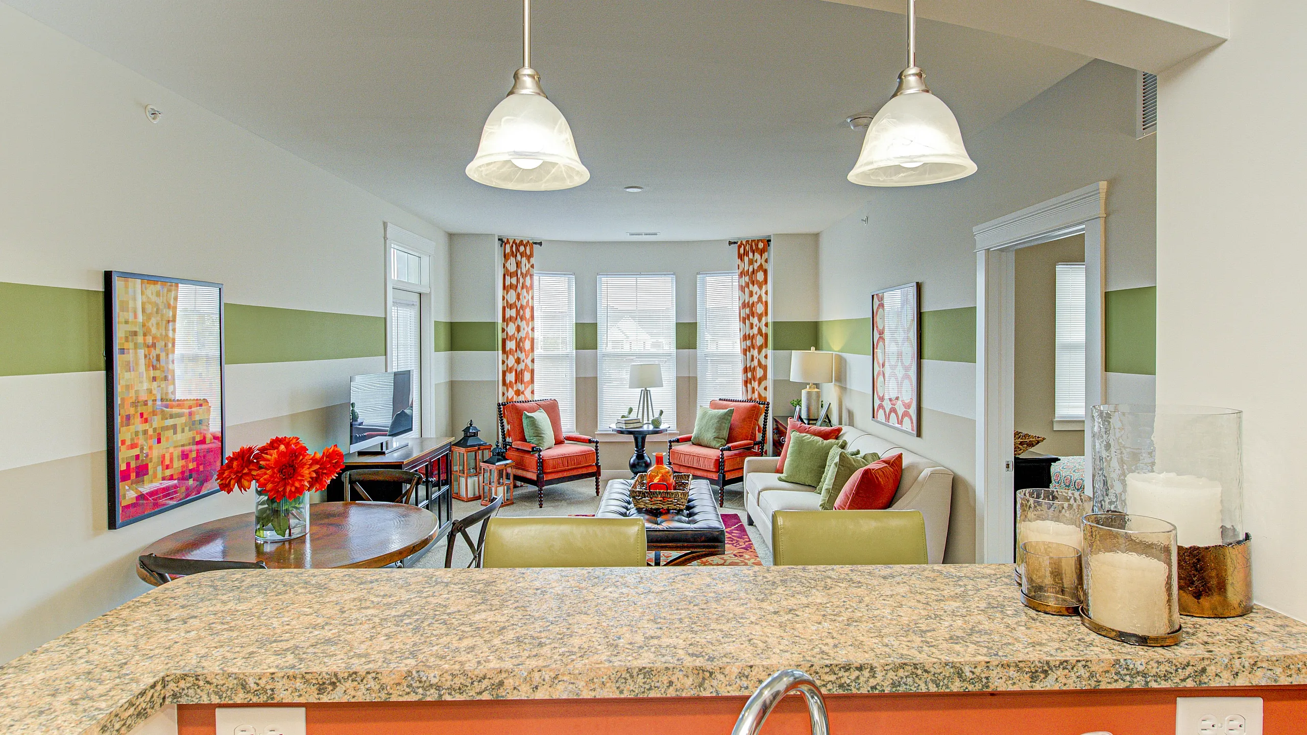 Inviting living room with vibrant decor, cozy seating, and large windows illuminating the space, viewed from a stylish granite kitchen counter.