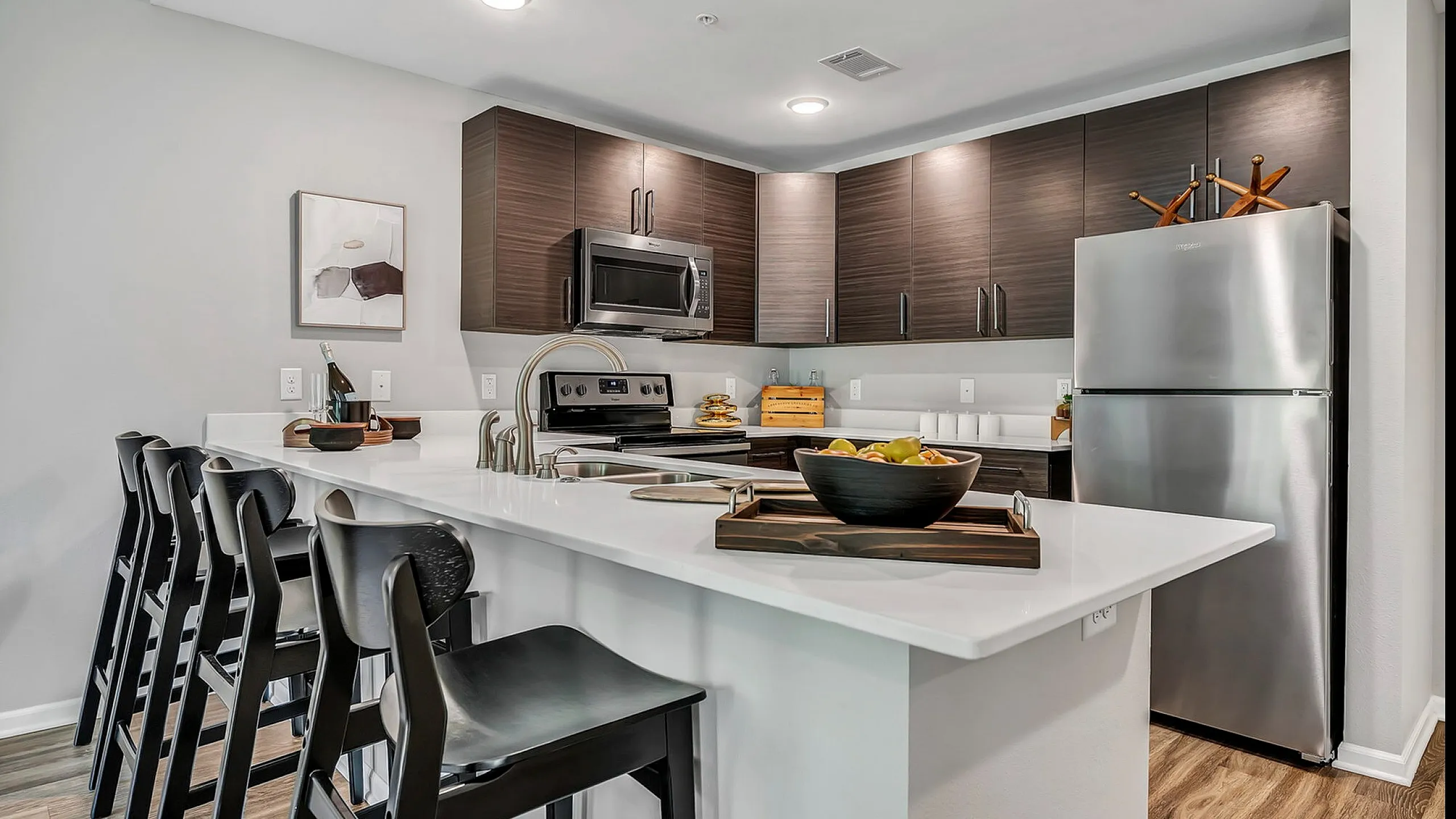 Modern kitchen featuring sleek dark wood cabinets, stainless steel appliances, and a stylish breakfast bar with elegant seating.