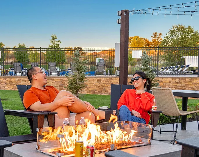 Inviting outdoor space with a cozy fire pit surrounded by comfortable seating, perfect for socializing and relaxation against a backdrop of lush greenery and a clear evening sky.