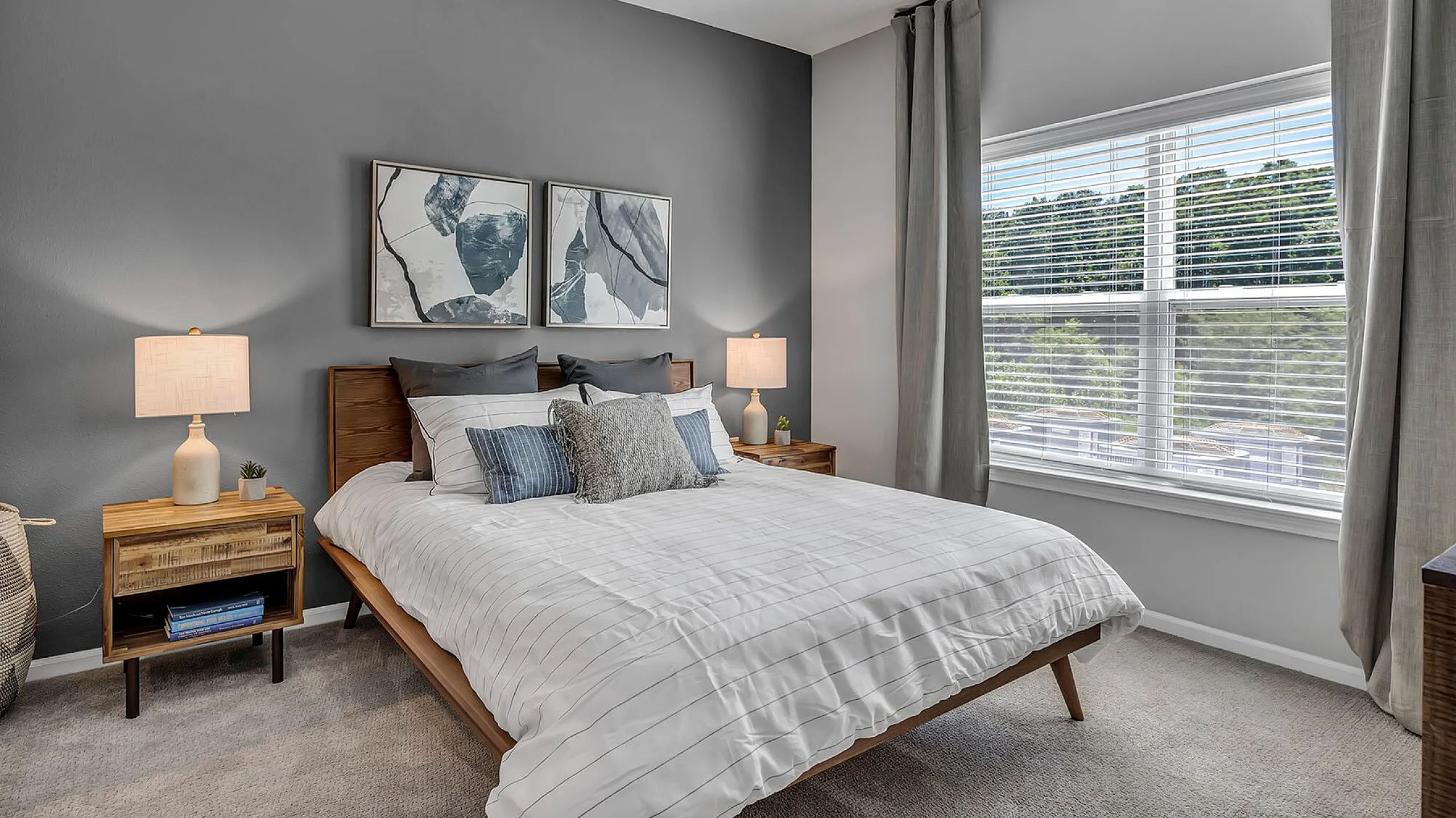 Inviting bedroom with modern decor, plush bedding, stylish gray accent wall, large window with natural light, and elegant wooden furniture.