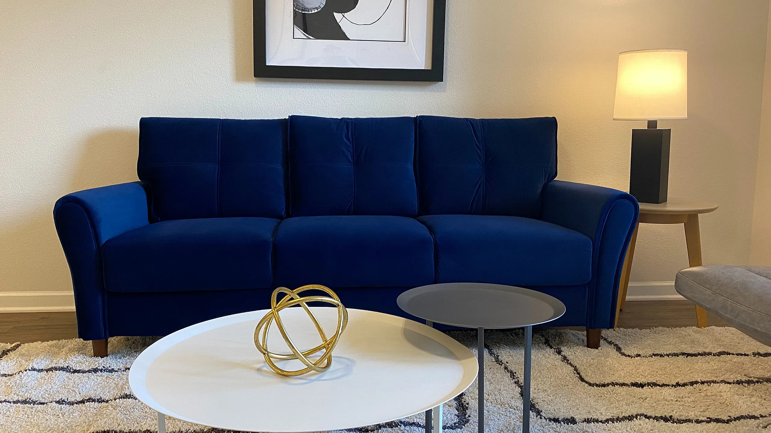 Modern living room featuring a plush blue sofa, stylish two-tone coffee tables, and elegant decor with warm lighting.
