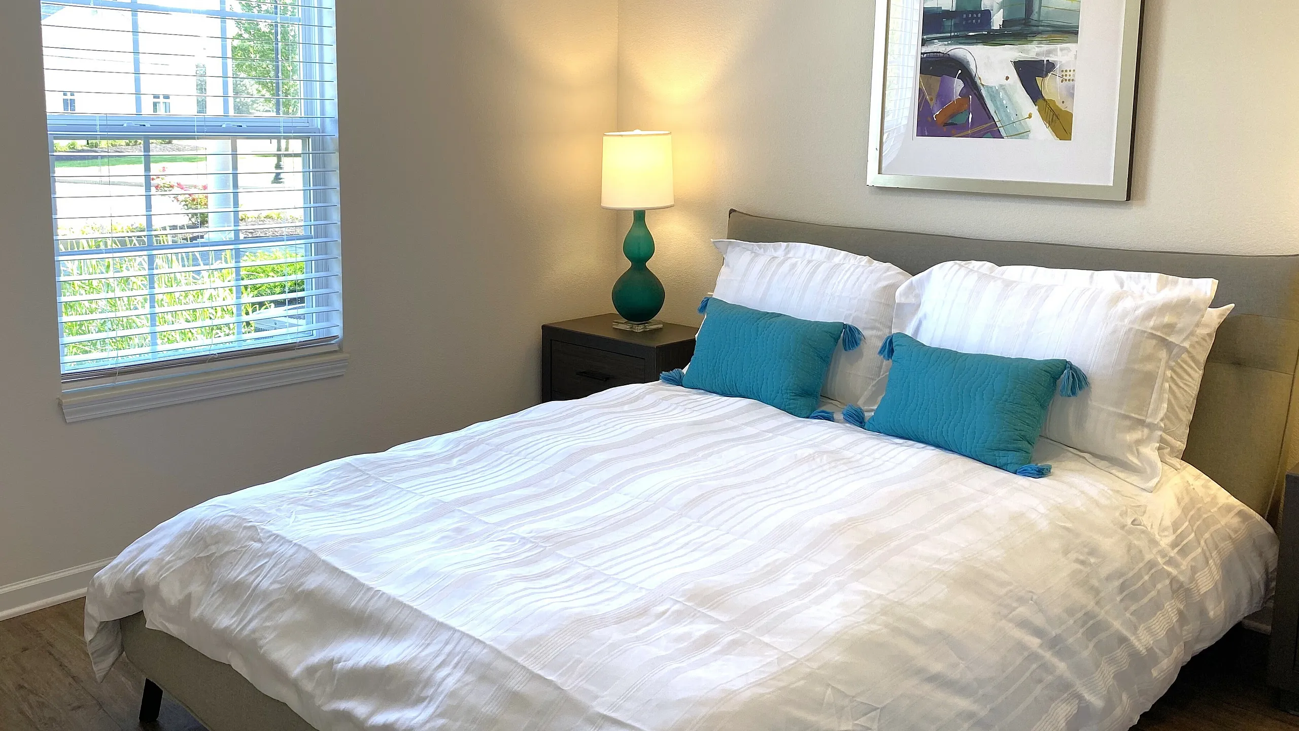 Bright and cozy bedroom with elegant decor, featuring a comfortable bed with plush pillows, a modern lamp, and a large window letting in natural light.