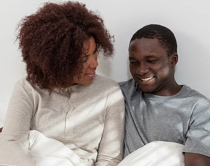 Happy couple comfortably sitting together in bed, using a laptop and enjoying a cozy and relaxed atmosphere.