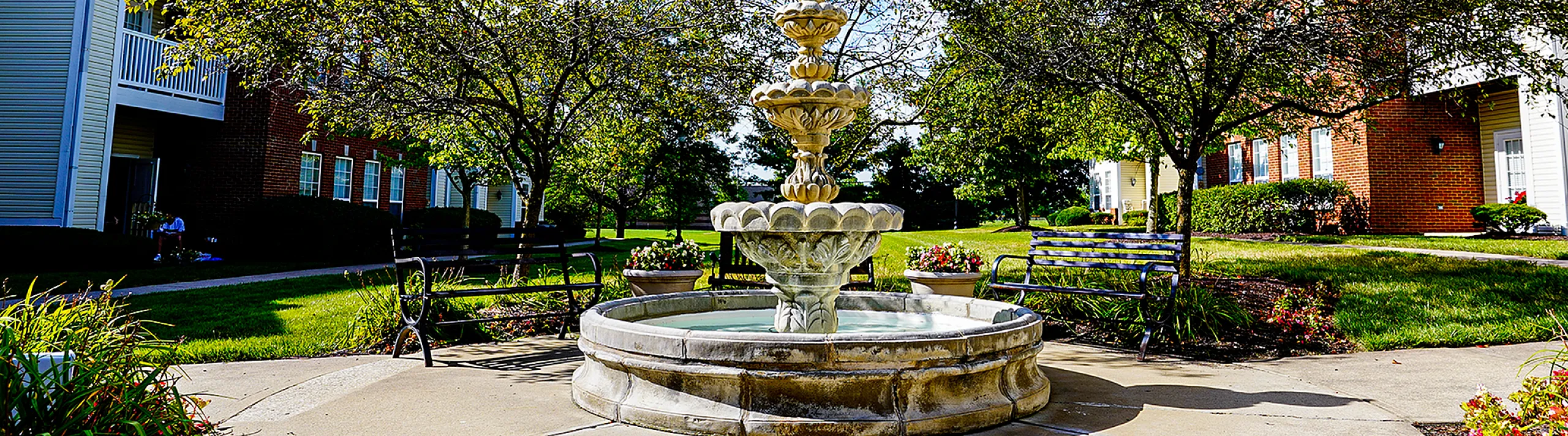 Charming courtyard with a central stone fountain surrounded by blooming greenery and cozy benches, set against a backdrop of elegant residential buildings.
