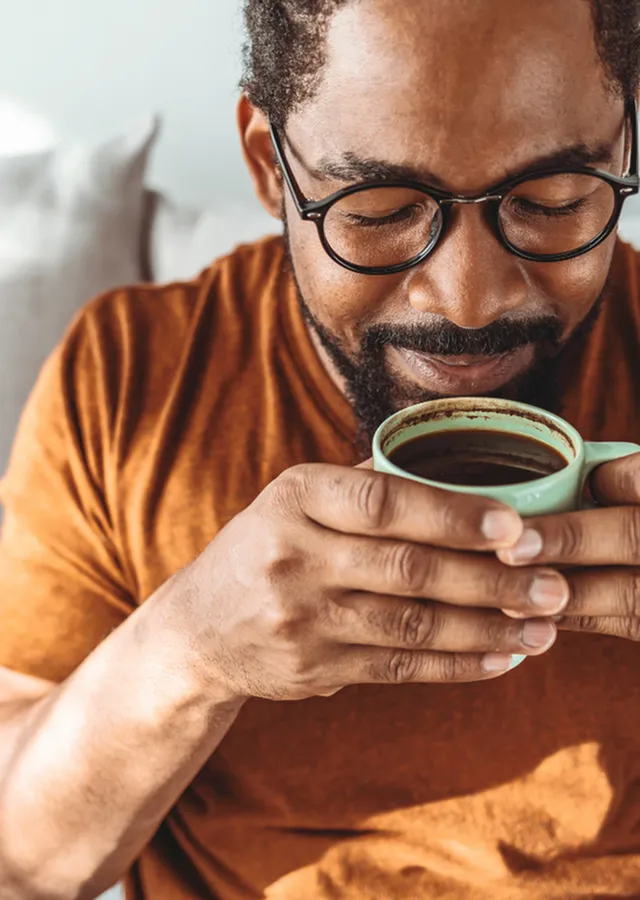 Man smiling and holding a warm cup of coffee while relaxing in a bright, modern indoor lounge with cozy seating.
