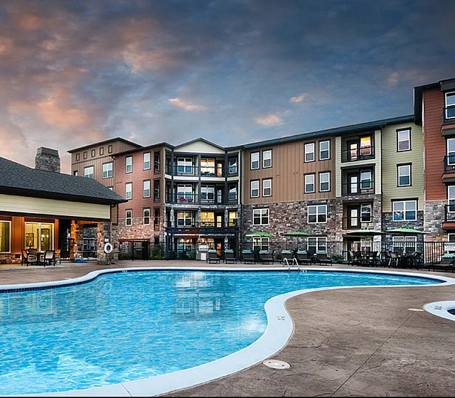 Charming apartment complex with a large, inviting swimming pool, surrounded by modern architecture and a serene evening sky.