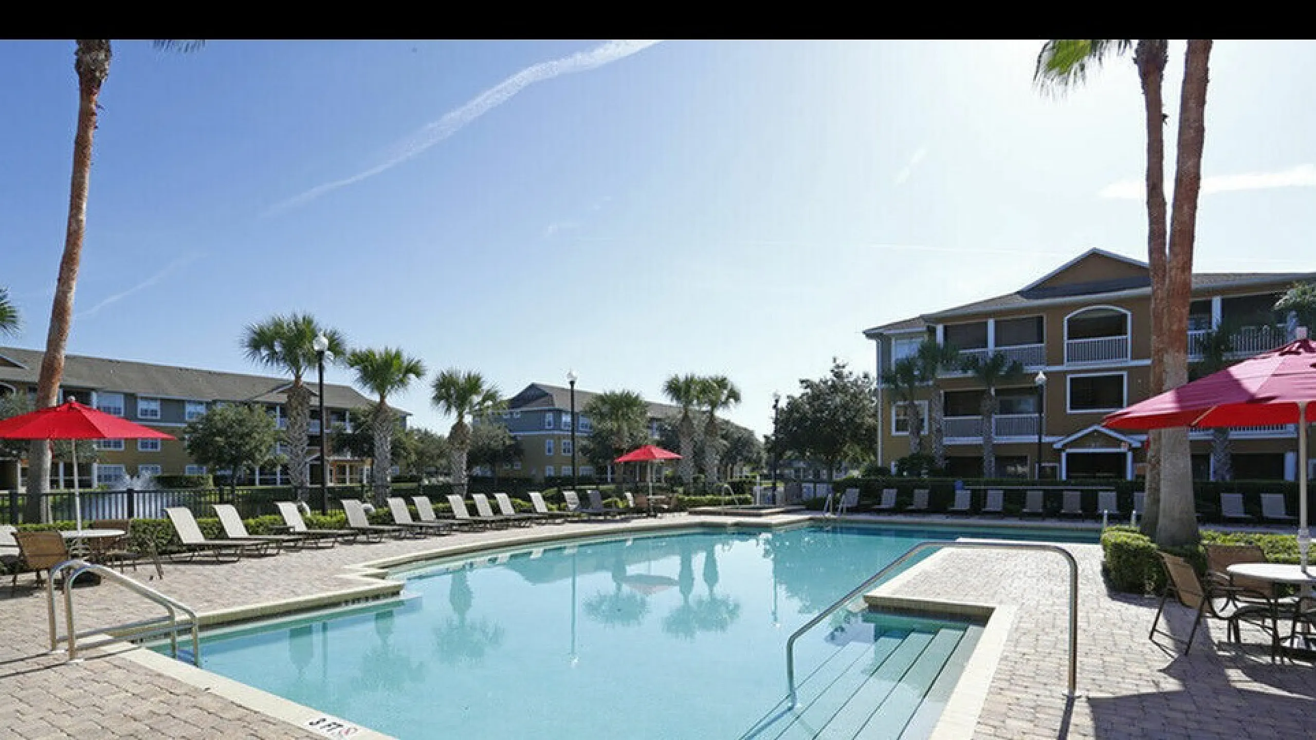 Inviting outdoor swimming pool surrounded by palm trees and sun loungers at a modern apartment complex.