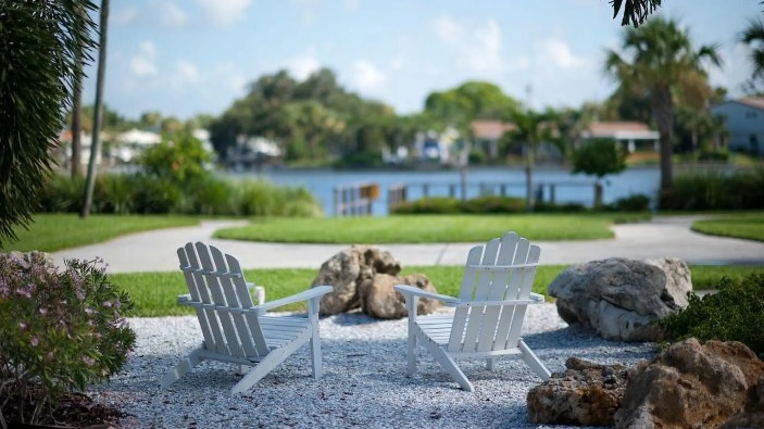Charming outdoor scene with two white Adirondack chairs facing a tranquil lake surrounded by lush greenery.