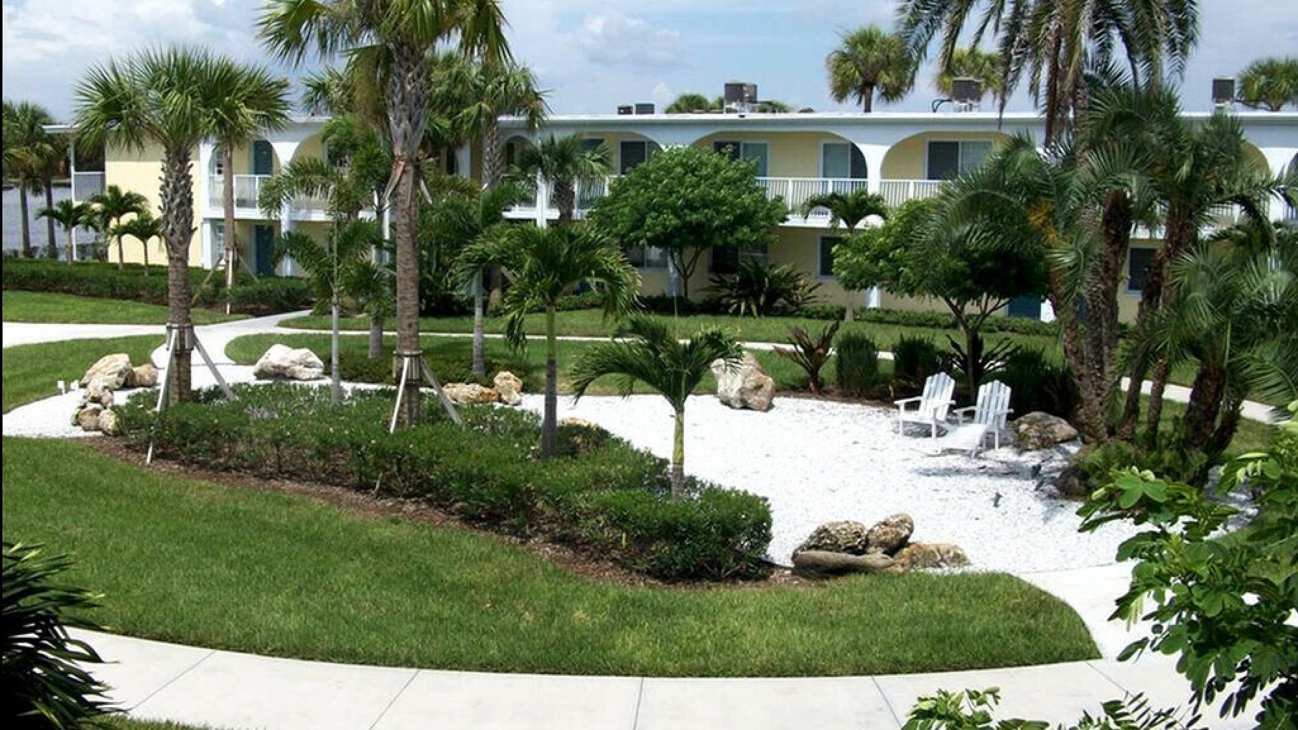 Lush apartment exterior featuring vibrant palm trees, well-maintained gardens, and a tranquil outdoor seating area.