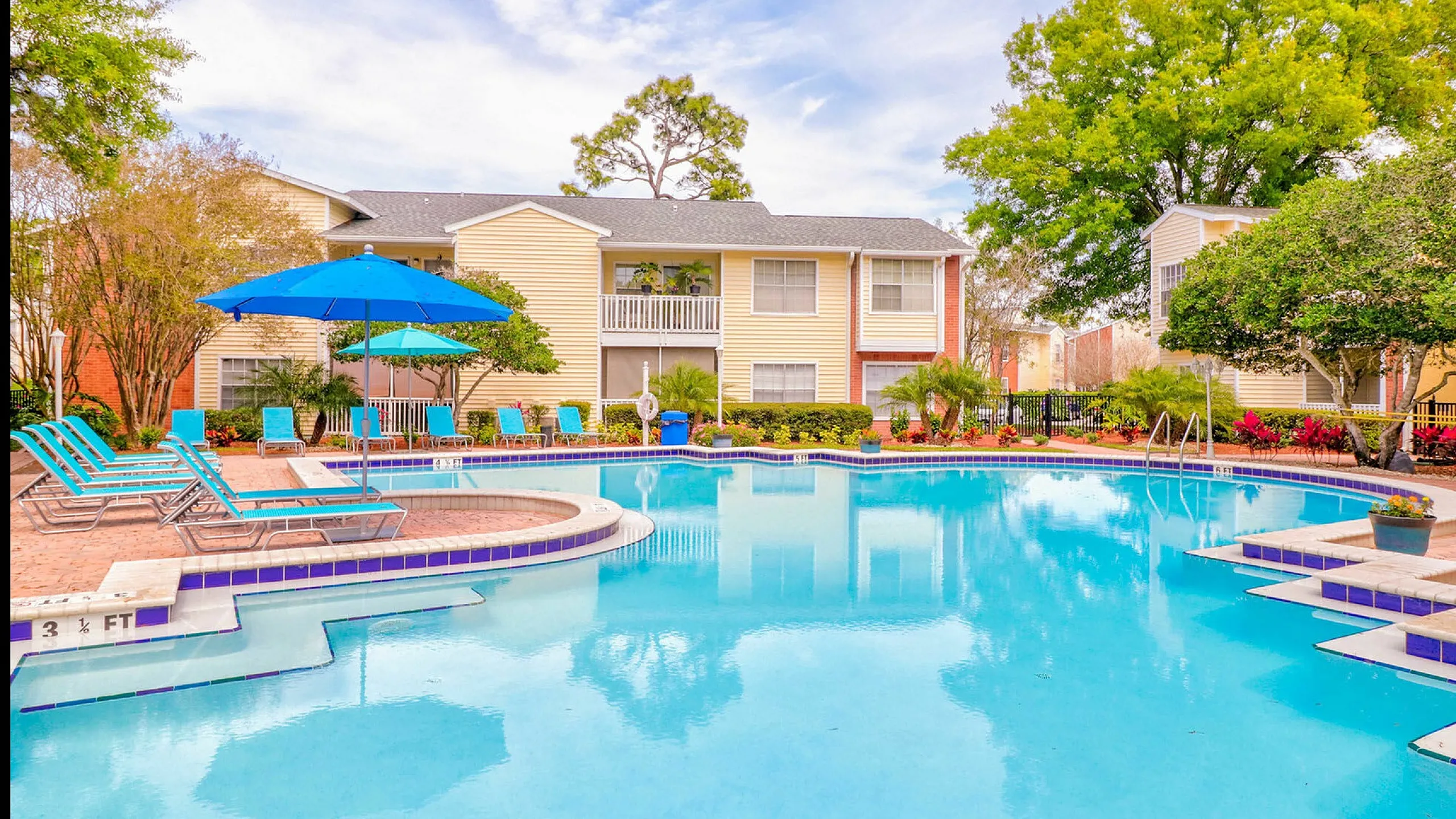 Inviting swimming pool with bright blue lounge chairs and umbrellas in a serene apartment complex.