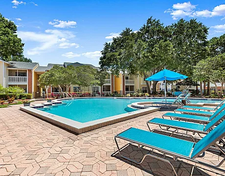 Idyllic pool area with sun loungers and umbrellas, surrounded by lush greenery and apartment buildings.