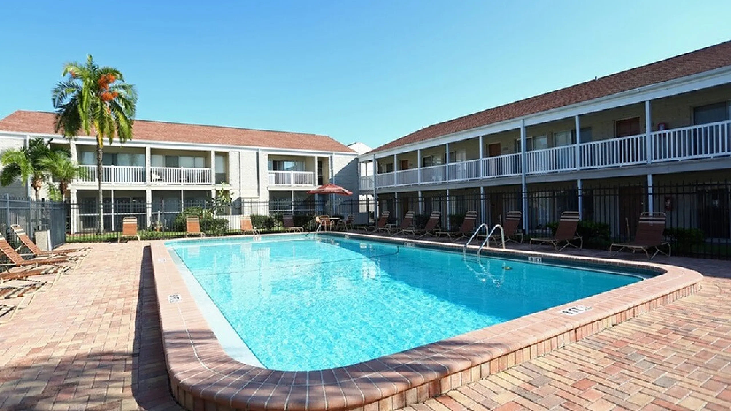 Spacious outdoor swimming pool surrounded by lounge chairs and apartment buildings.