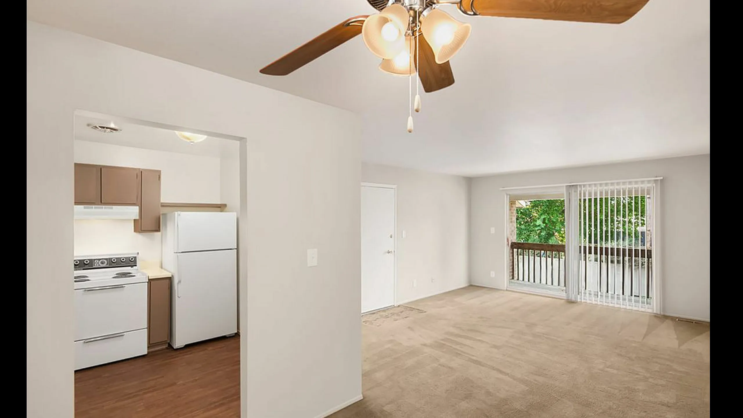 Bright open-concept living room with a ceiling fan, sliding door, and adjacent kitchen space.