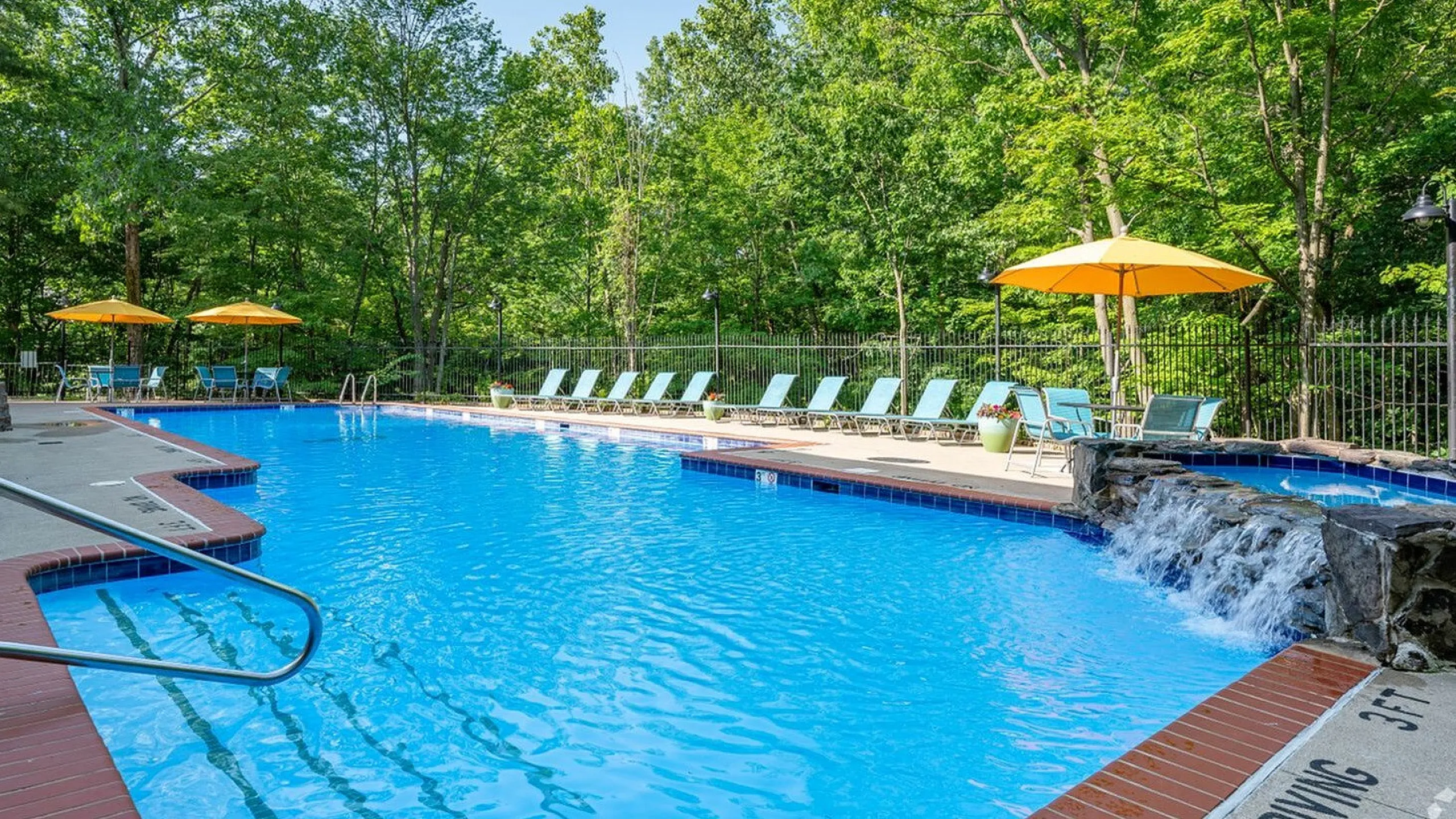 Inviting outdoor pool area with vibrant blue water, surrounded by lush greenery and stylish lounge chairs featuring bright yellow umbrellas.
