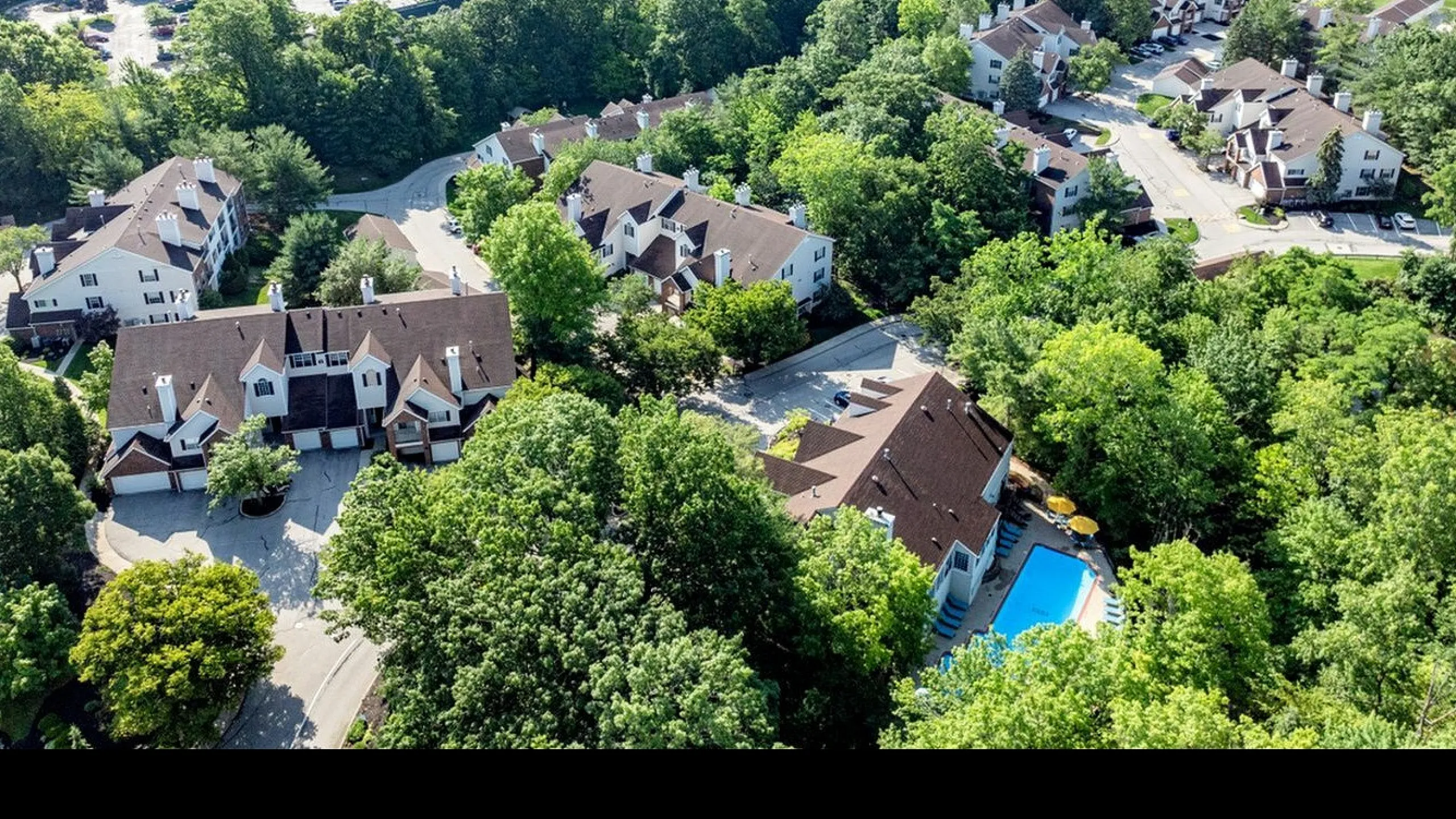 Charming aerial view of a serene, tree-lined residential community with a refreshing swimming pool, highlighting peaceful living surrounded by lush greenery.