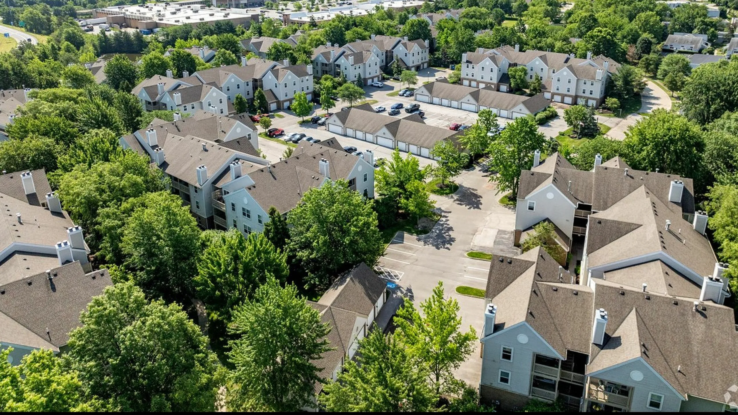 Scenic aerial view of stylish suburban apartment complex surrounded by lush greenery and open spaces.