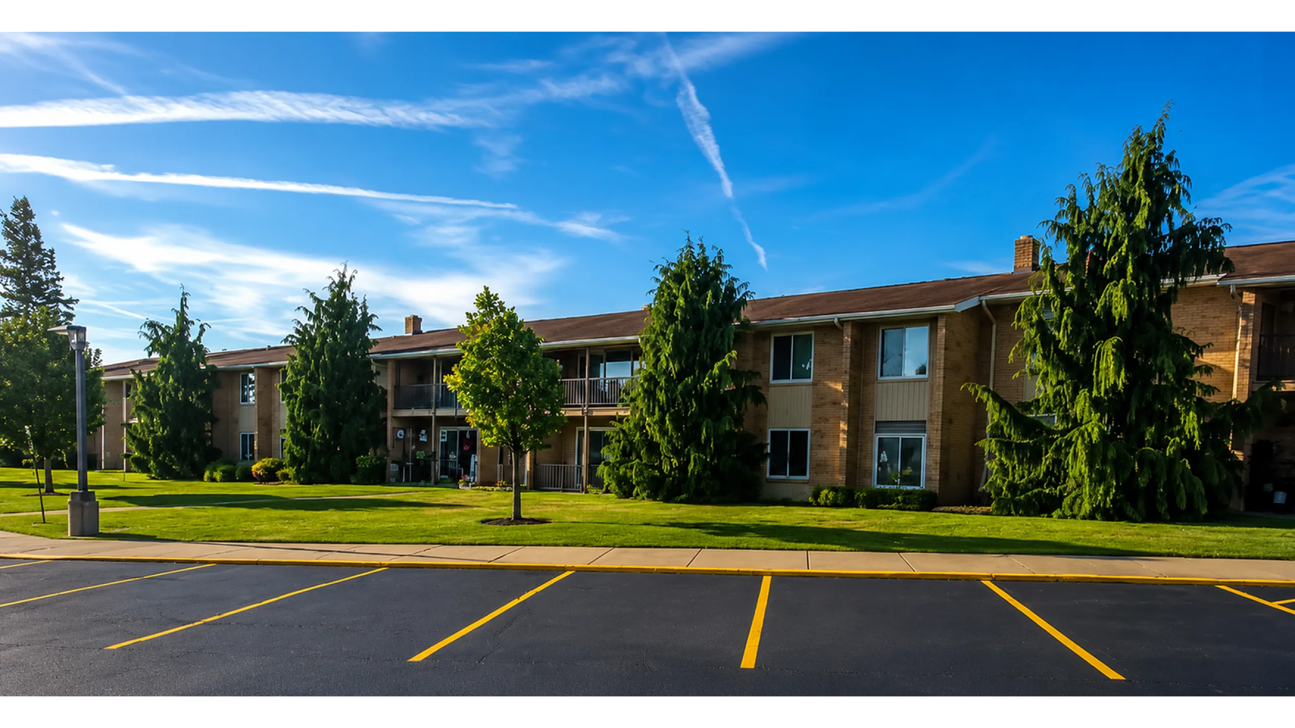 Charming suburban apartment complex surrounded by lush green landscaping and vibrant trees under a clear blue sky.