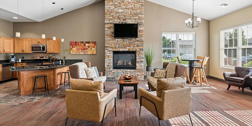 Modern living area with spacious open-concept kitchen, elegant stone fireplace, and large windows offering abundant natural light.