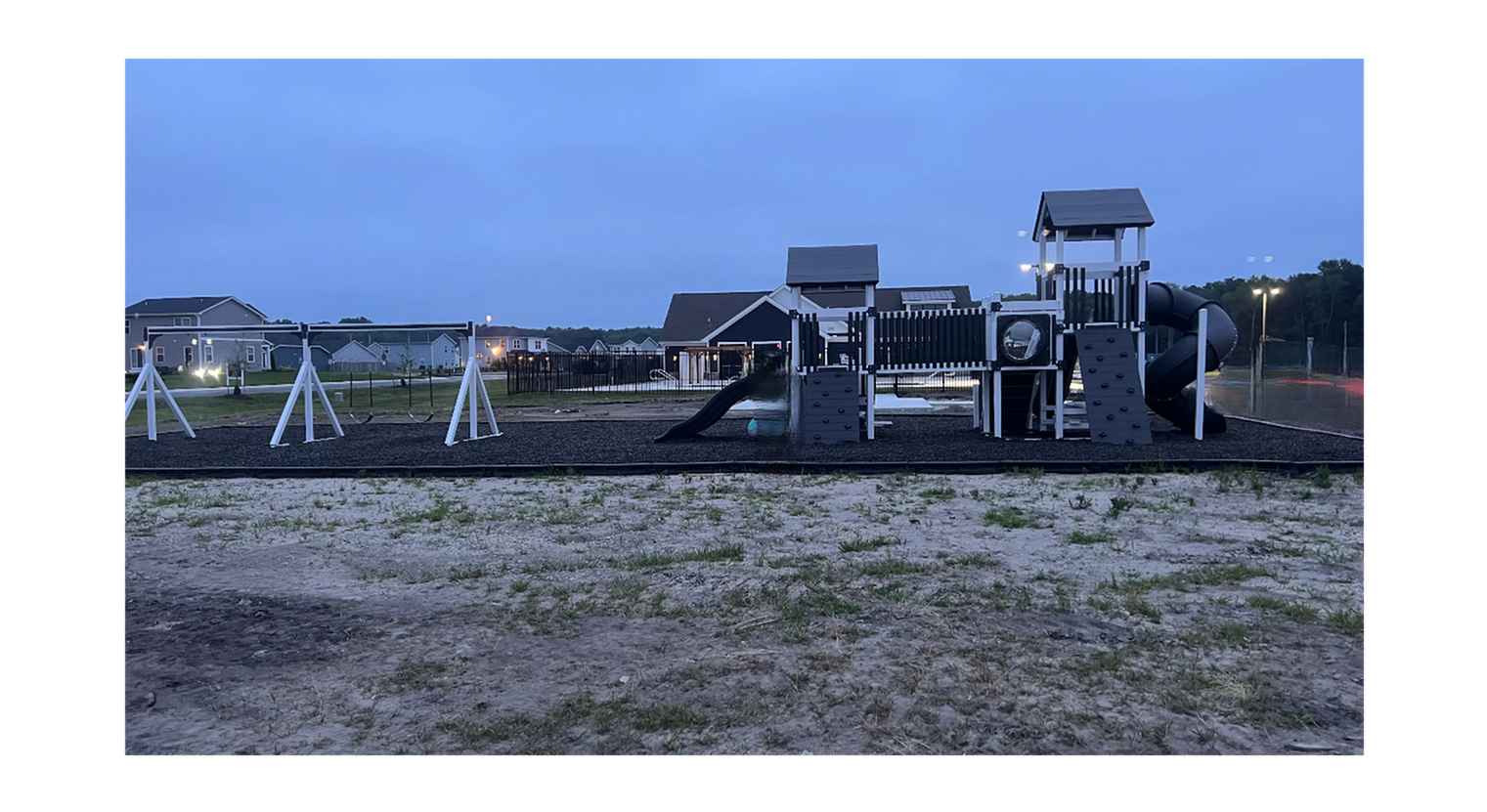 Charming playground area with swings and a modern play structure, nestled in a quiet residential community at dusk.