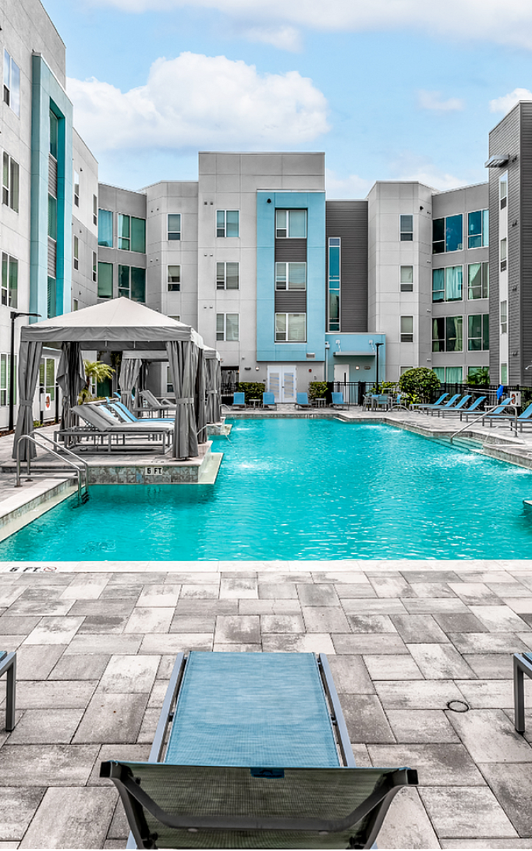 Modern apartment complex courtyard with a luxurious swimming pool, surrounded by stylish sun loungers and vibrant landscaping.