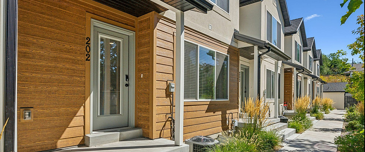 Modern townhouse row with sleek architectural design, warm wood accents, and lush landscape under a clear blue sky.