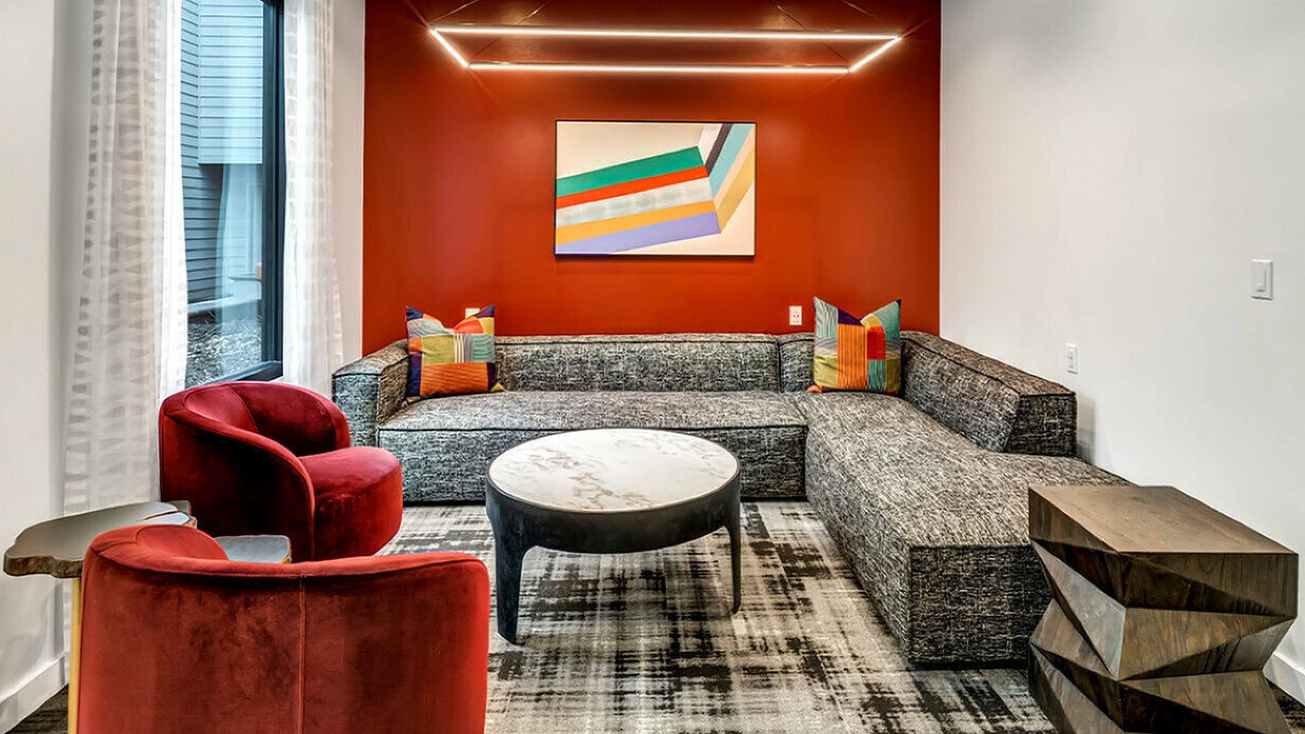 Modern lounge with vibrant red accent wall, abstract artwork, and luxurious seating.