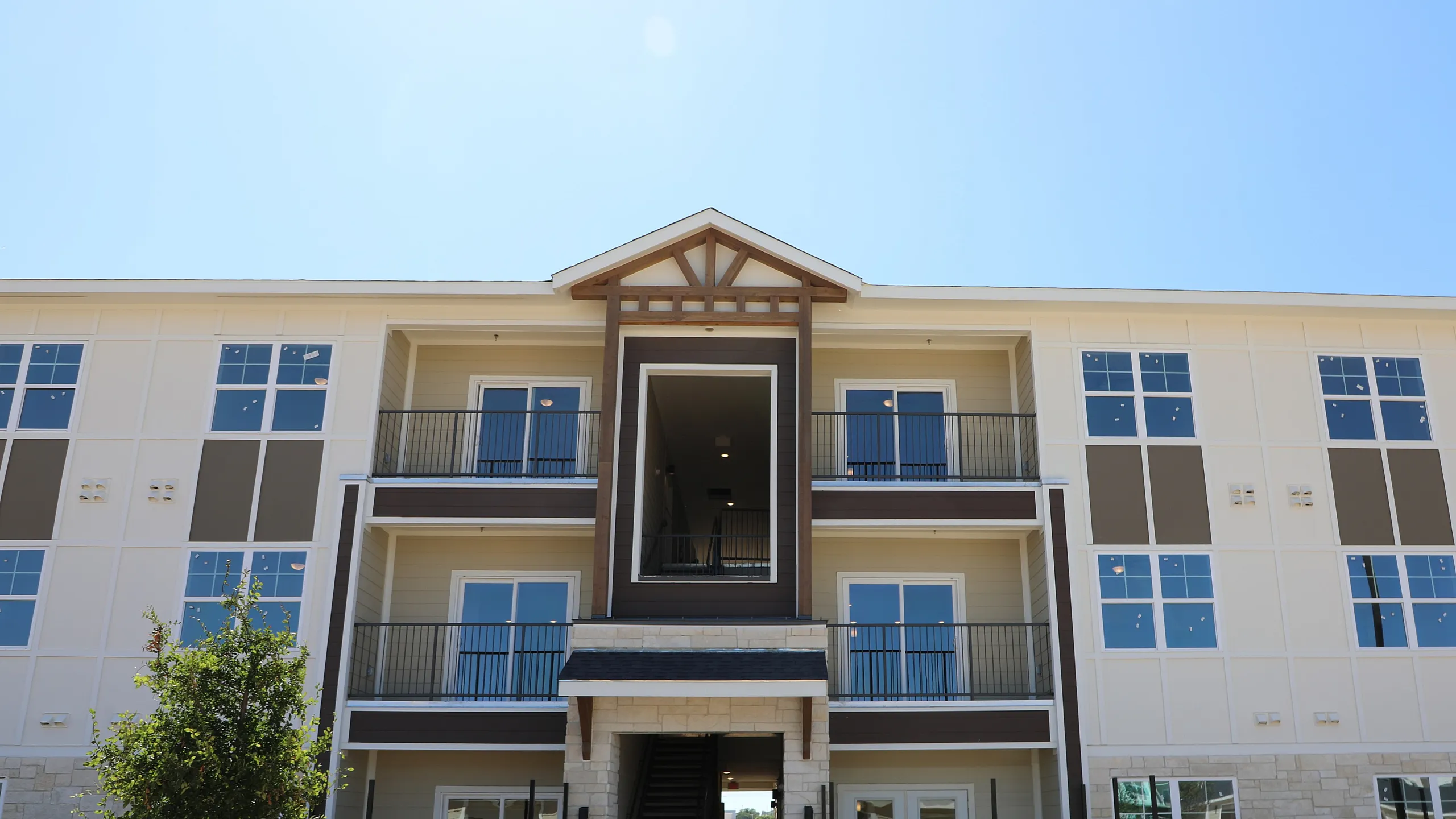 Modern three-story apartment building with spacious balconies, large windows, and elegant architectural details set against a clear blue sky.