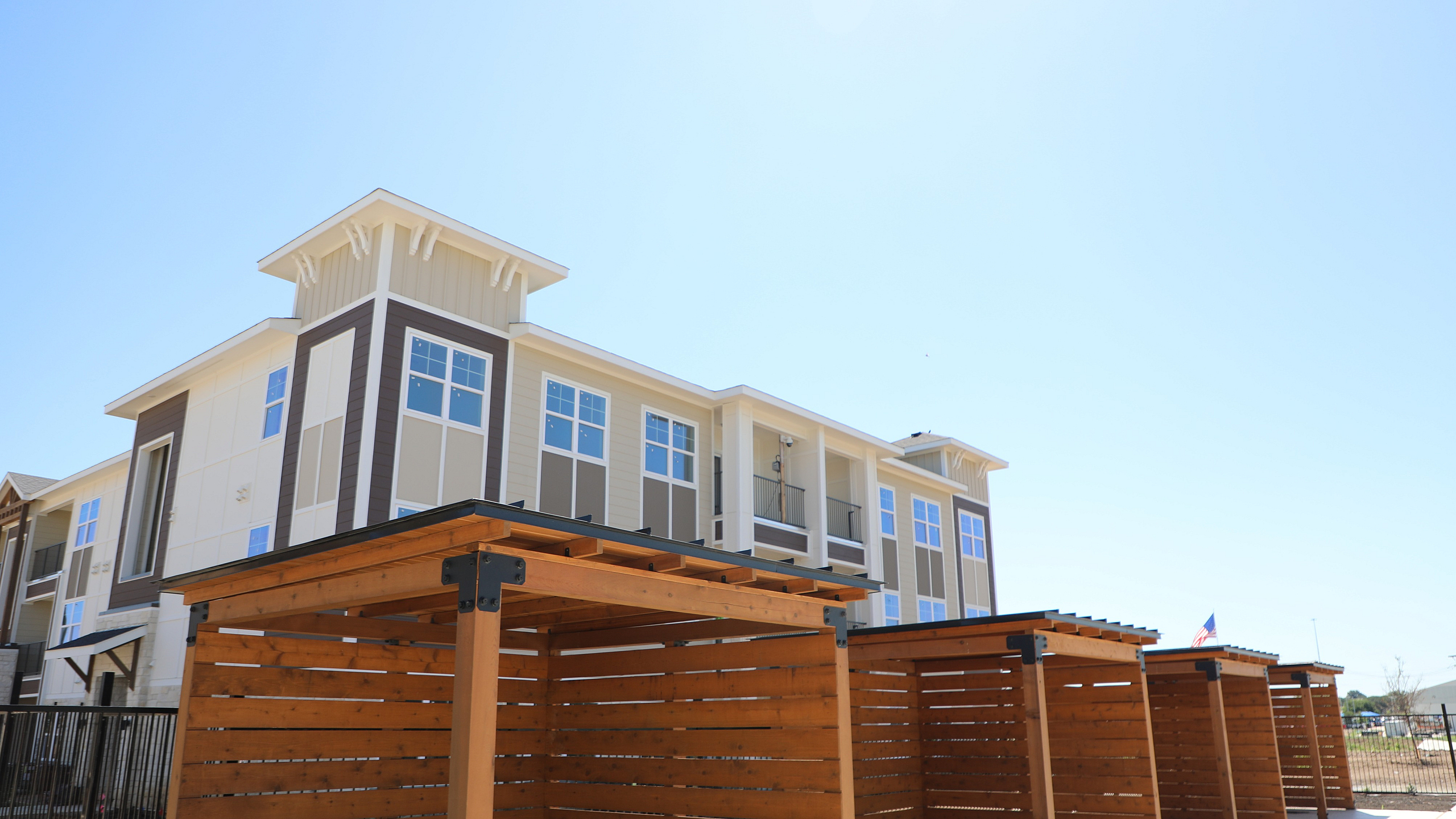 Modern apartment building with elegant architecture, large windows, and stylish wooden carports under a clear blue sky.