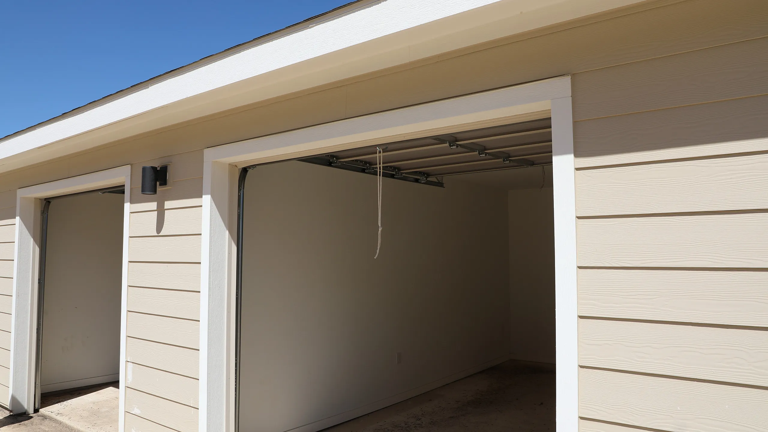 Bright and spacious double garage with modern beige siding and open doors, showcasing ample storage potential.