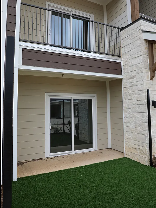 Charming apartment exterior with modern stone and wood accents, featuring a cozy patio and lush green artificial turf.