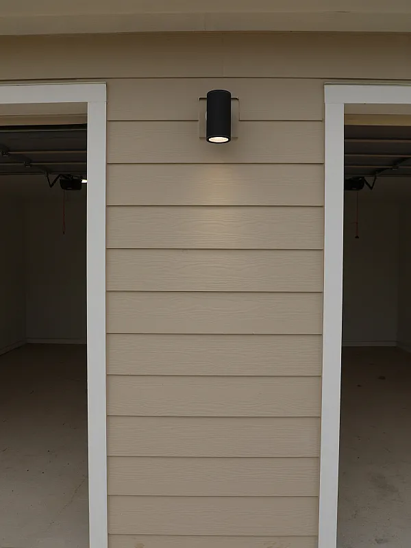 Elegant garage exterior with modern beige paneling and a sleek black wall light for a contemporary appeal.