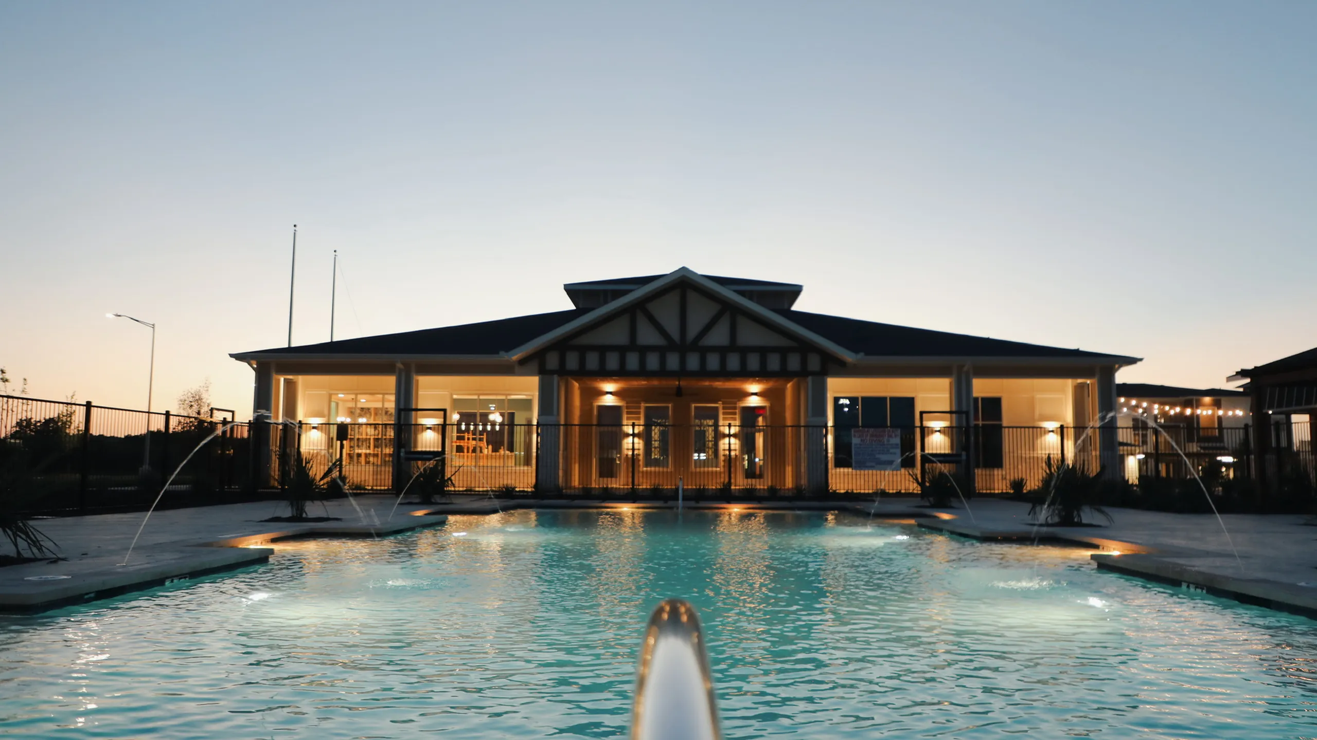 Resort-style pool with bubbler fountains at dusk in front of the illuminated clubhouse at The Entrada at San Marcos