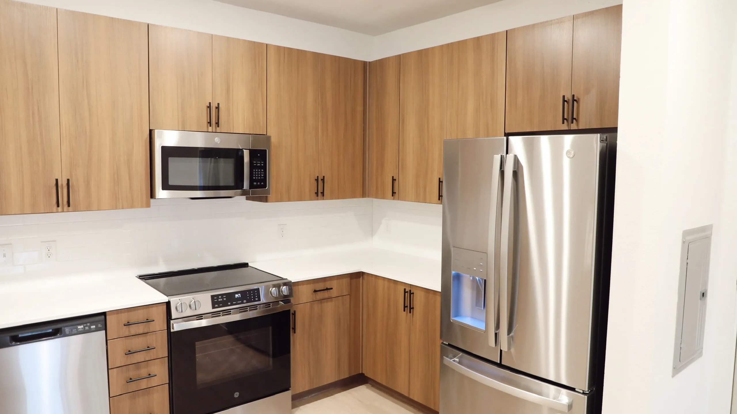 Modern kitchen with sleek stainless steel appliances, warm wooden cabinets, and pristine white countertops.