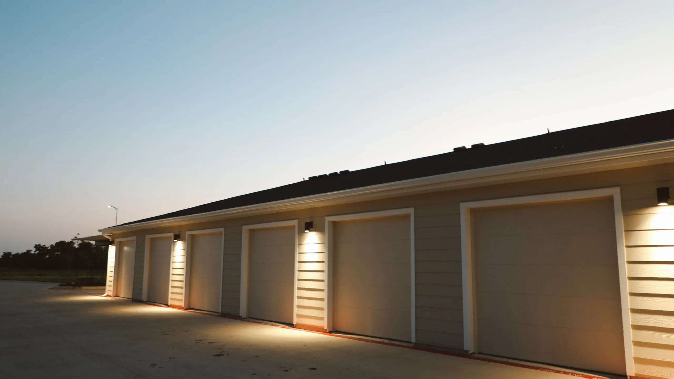 Modern residential garage with multiple doors, warmly lit at dusk, showcasing secure and spacious storage solutions.
