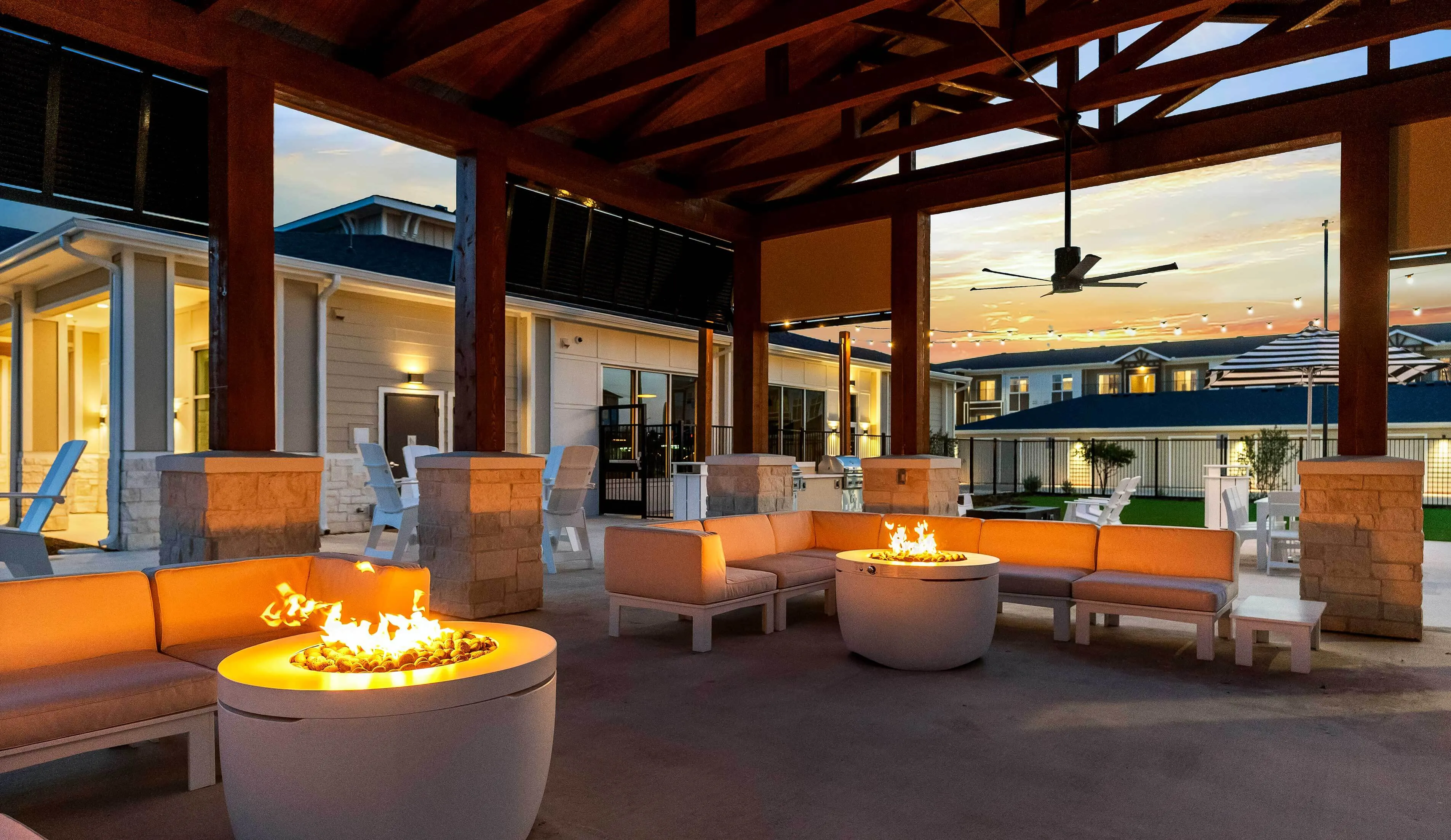 Charming outdoor lounge at sunset featuring cozy fire pits, elegant seating, and modern architecture for a perfect evening gathering.