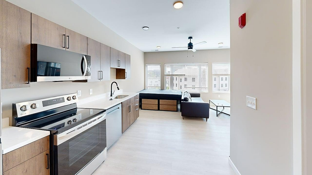 Modern open-concept apartment with sleek kitchen, featuring stainless steel appliances, wooden cabinets, and a spacious living area with large windows for natural light.