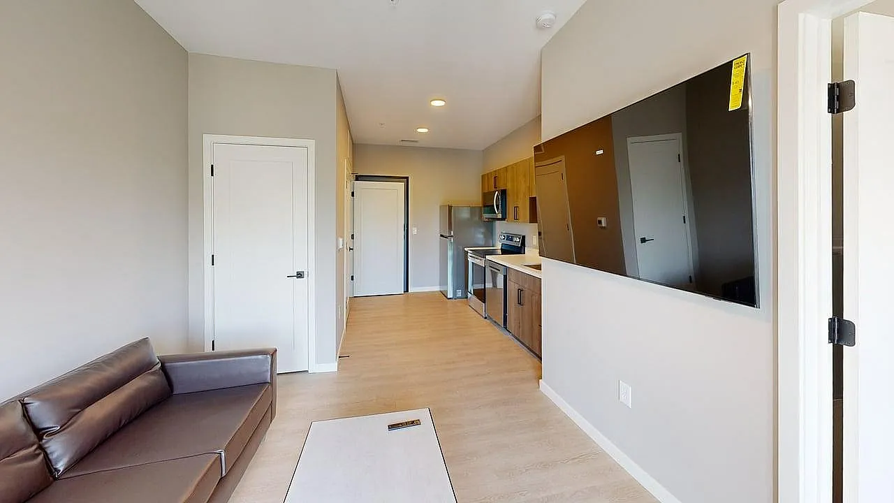 Modern apartment interior with sleek kitchen, comfortable sofa, and large wall-mounted TV, featuring spacious layout and contemporary design.