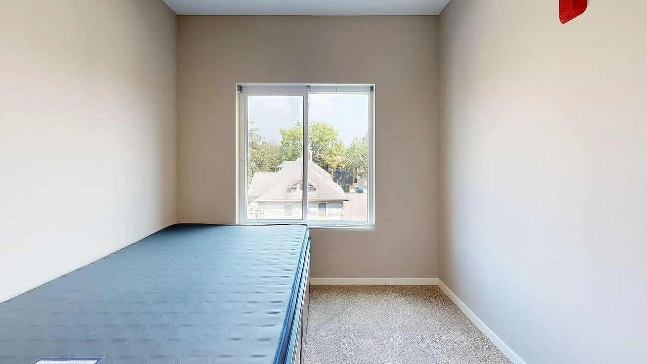 Bright bedroom with plush carpet flooring, featuring a large window offering a scenic view.